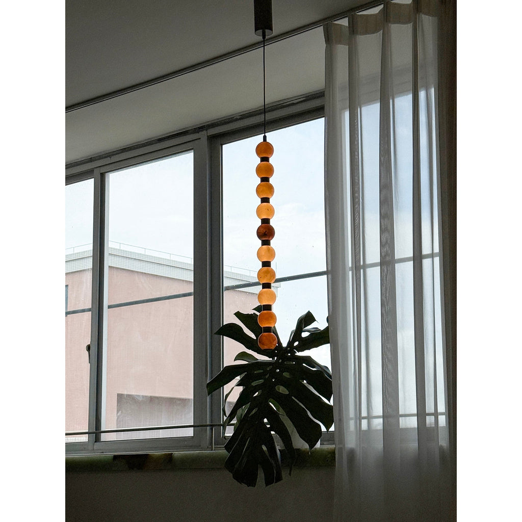 The stacked spheres of this Clérachic pendant glow warm orange against a window and rooftop view.