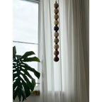 The pale natural stone tones of this Clérachic pendant hang beside a monstera leaf and sheer curtain.