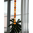 This Clérachic alabaster sphere pendant hangs against a window, a broad monstera leaf reaching up below it.