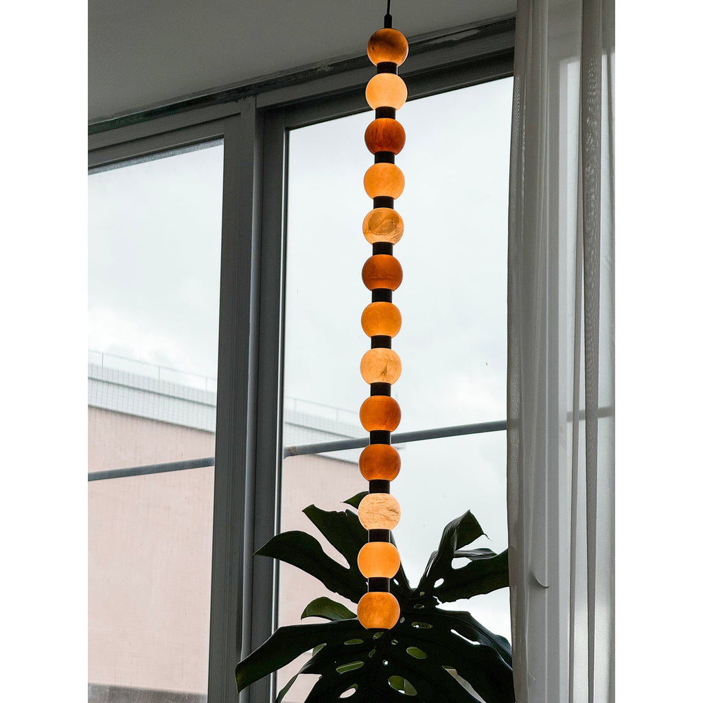 Warm light glows through the stacked spheres of this Clérachic pendant above a monstera leaf.