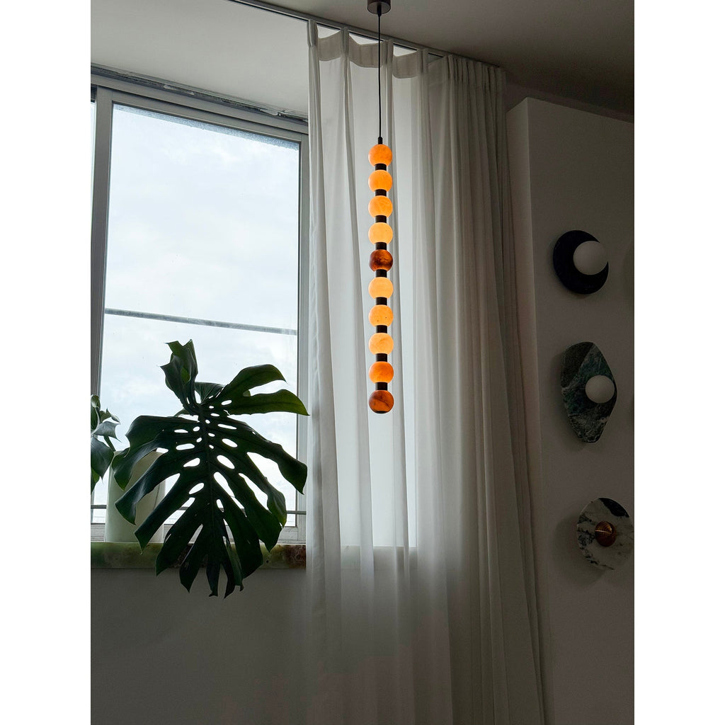 In dimmer light, this Clérachic pendant's spheres glow softly beside a curtained window and a wall of round discs.