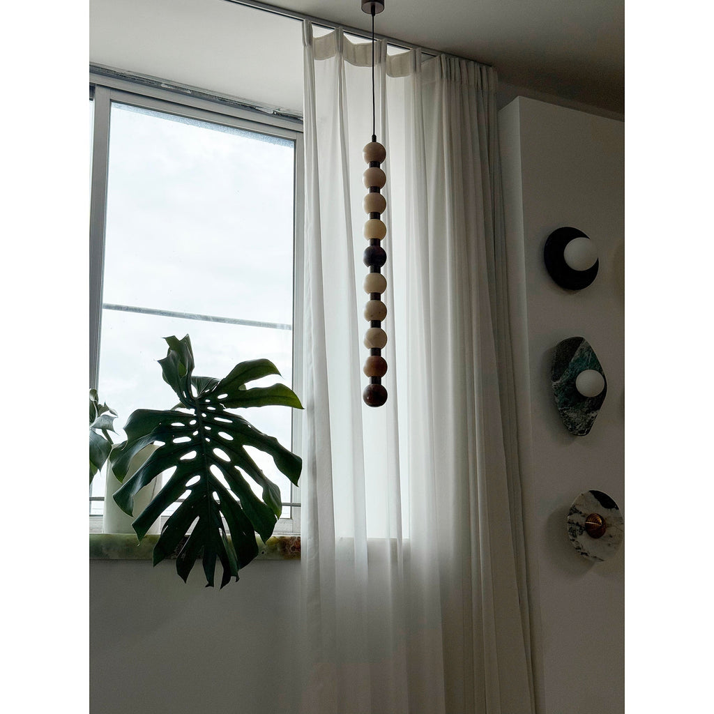 A close view shows the pale natural stone tones of this Clérachic pendant beside a wall of round discs.