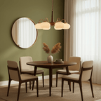 A four-light Clérachic chandelier hangs over a round dining table in a sage-green room with a wall mirror.