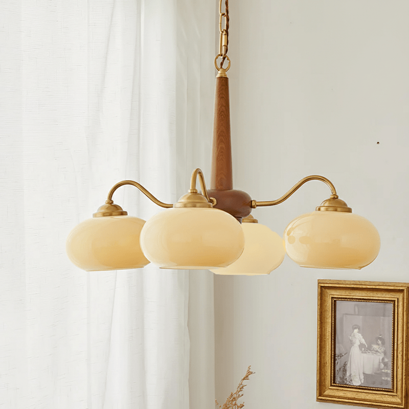 Visible wood grain shows on this Clérachic chandelier's pole, its four cream shades lit beside a gilt-framed print.