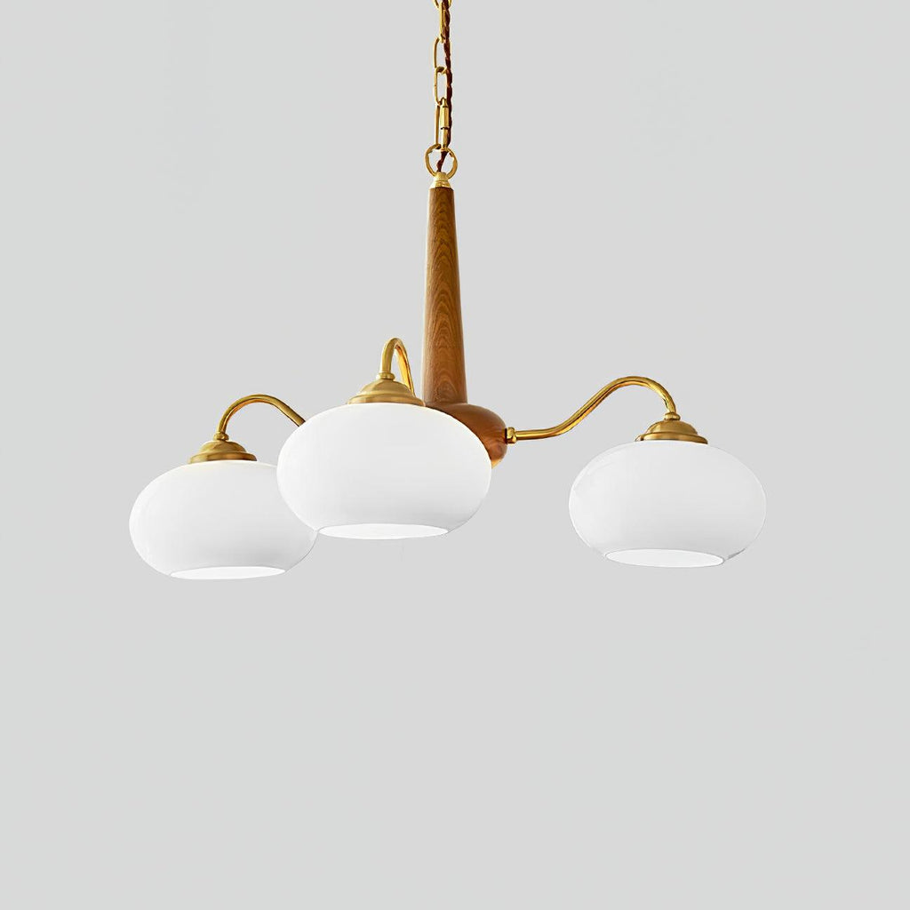Three white glass shades hang from the brass arms of this Clérachic chandelier against a grey backdrop.