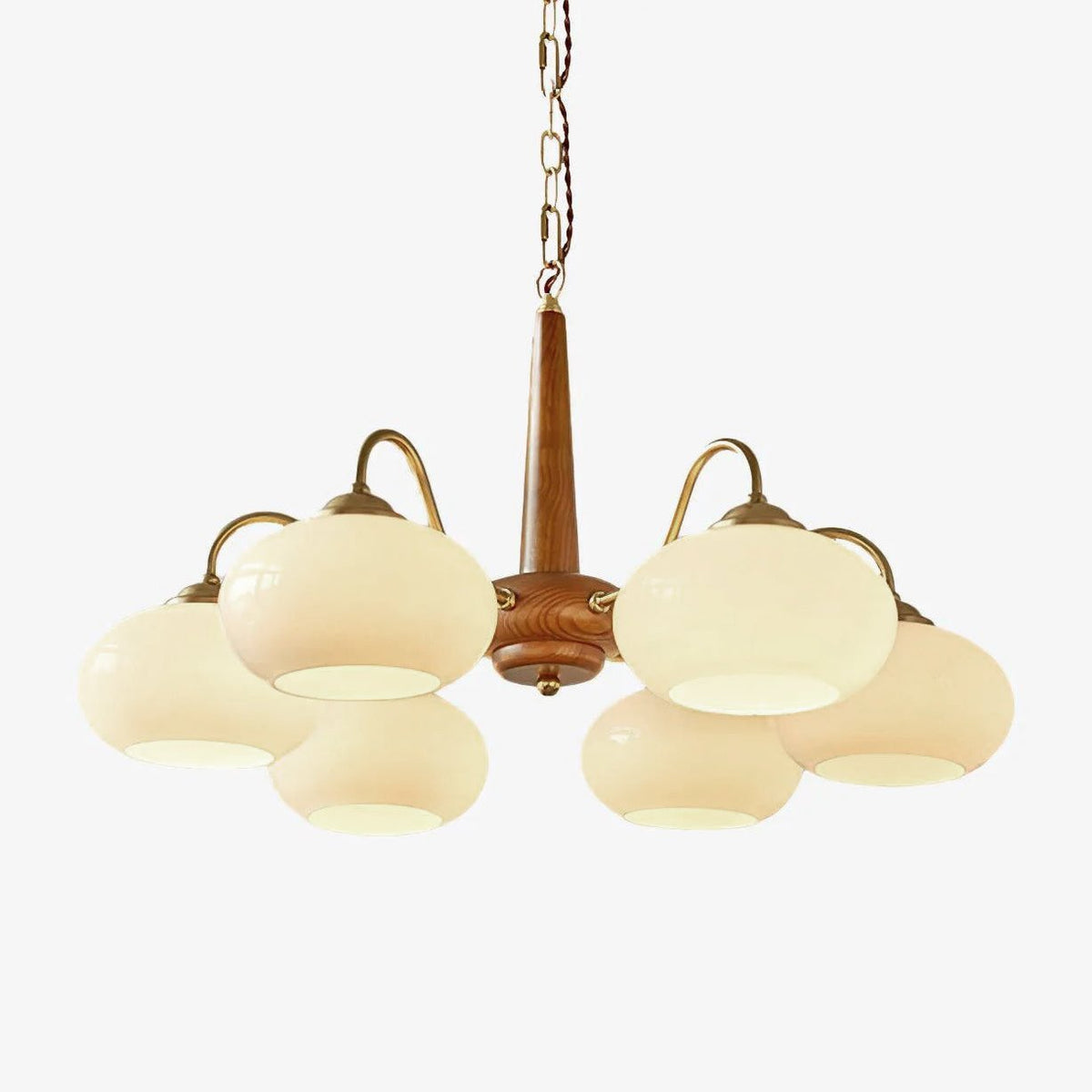 Photographed against white, this Clérachic chandelier's six cream glass shades sit on scrolled brass arms.