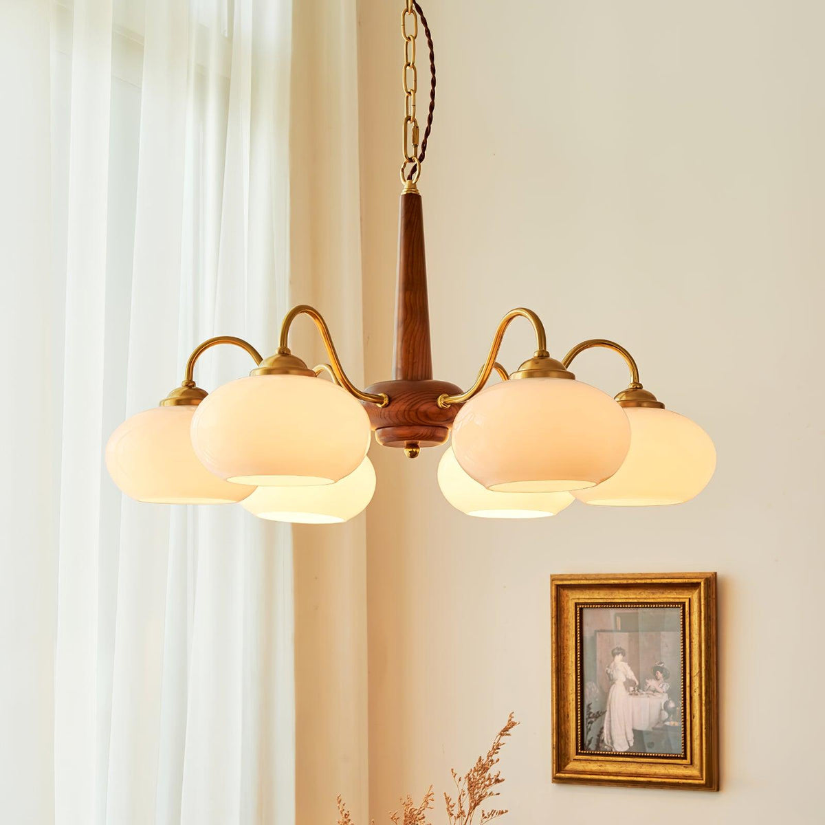 A six-light Clérachic chandelier with cream glass shades hangs beside sheer curtains and a framed vintage print.