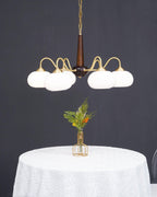 Unlit, this Clérachic chandelier's white glass shades are shown straight-on above a white-clothed round table.