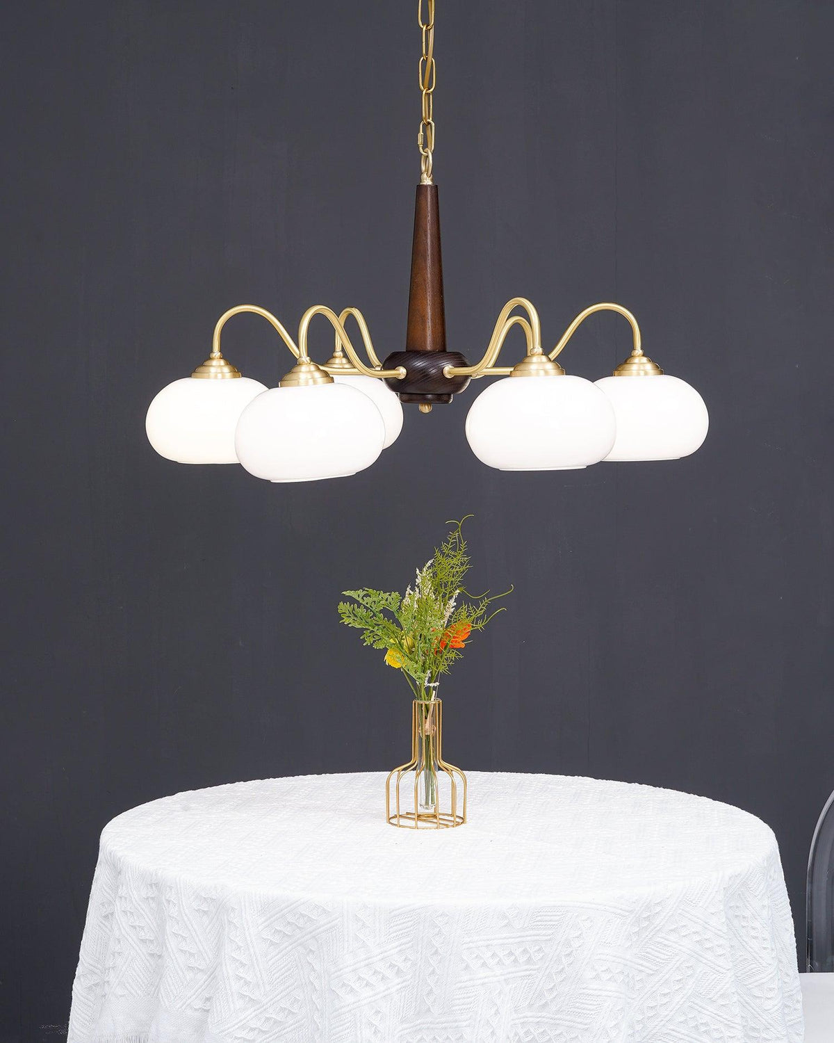 Unlit, this Clérachic chandelier's white glass shades are shown straight-on above a white-clothed round table.