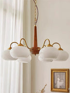 A gilt-framed vintage print hangs beside this Clérachic chandelier, its white shades bright against a pale wall.