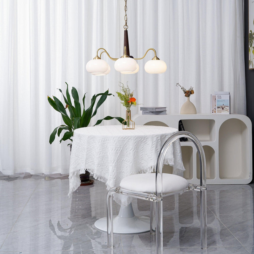 Beside a clear acrylic dining chair, this Clérachic chandelier's three white shades hang over a skirted round table.