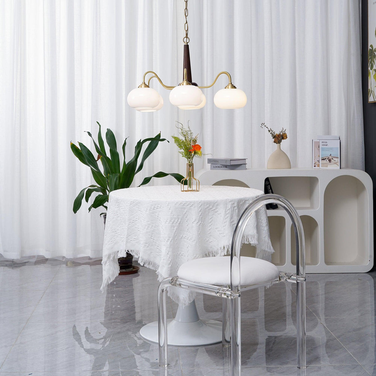 Beside a clear acrylic dining chair, this Clérachic chandelier's three white shades hang over a skirted round table.