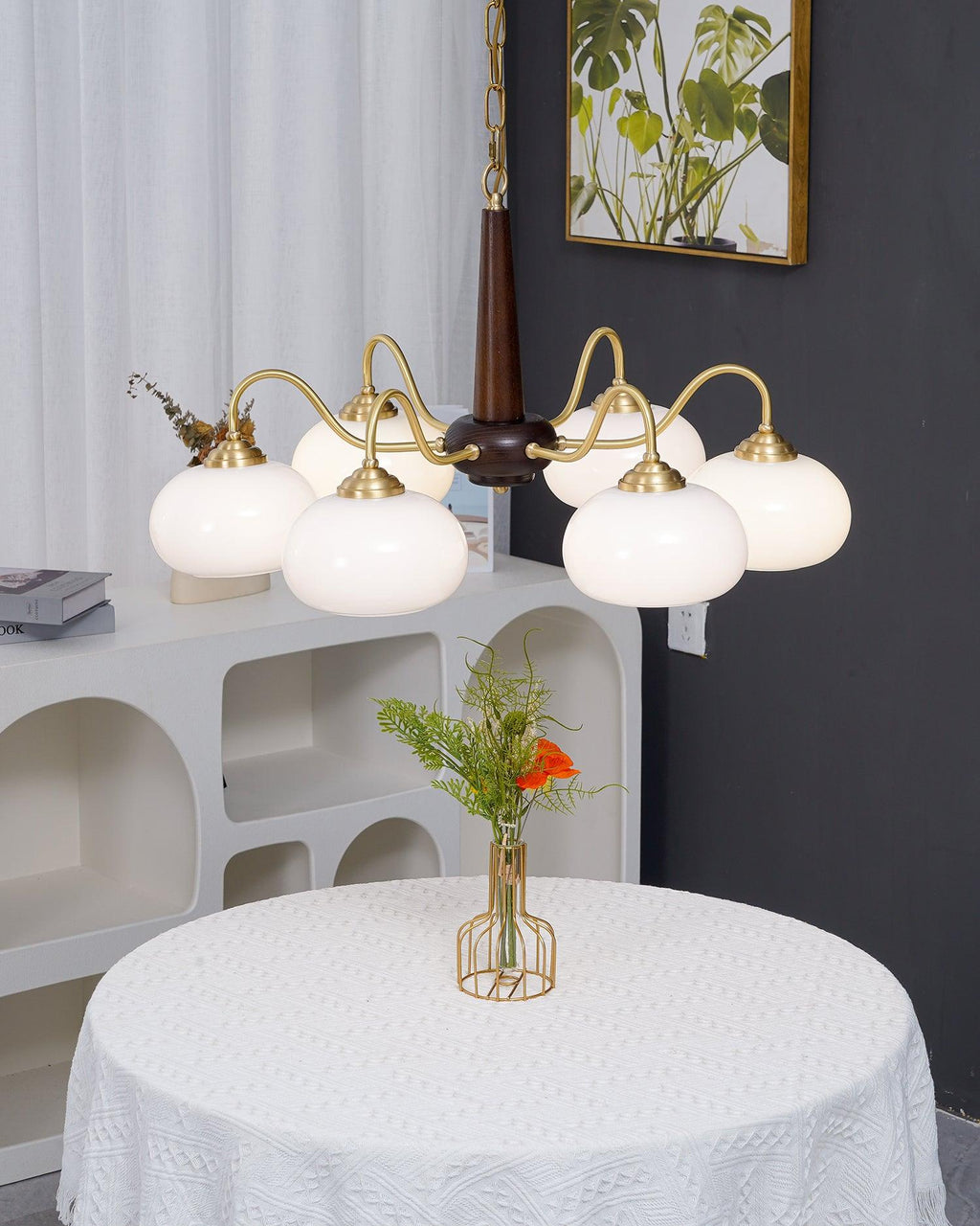 White glass shades on this Clérachic chandelier hang over a round table dressed in white, against a dark wall.