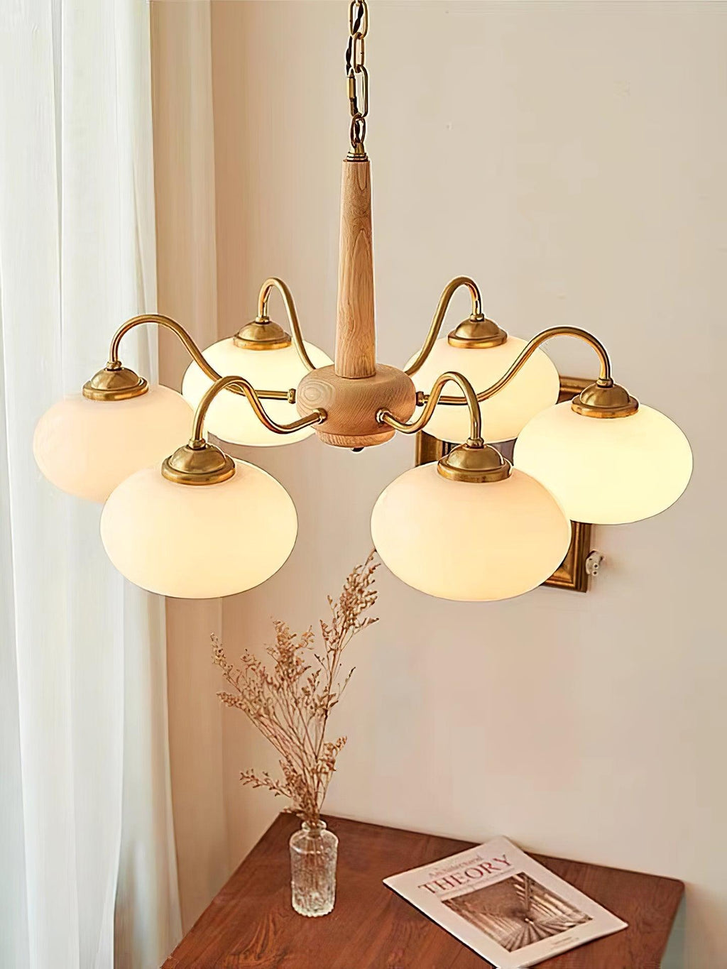 A magazine rests on a wood side table beneath this Clérachic chandelier's outstretched brass arms.