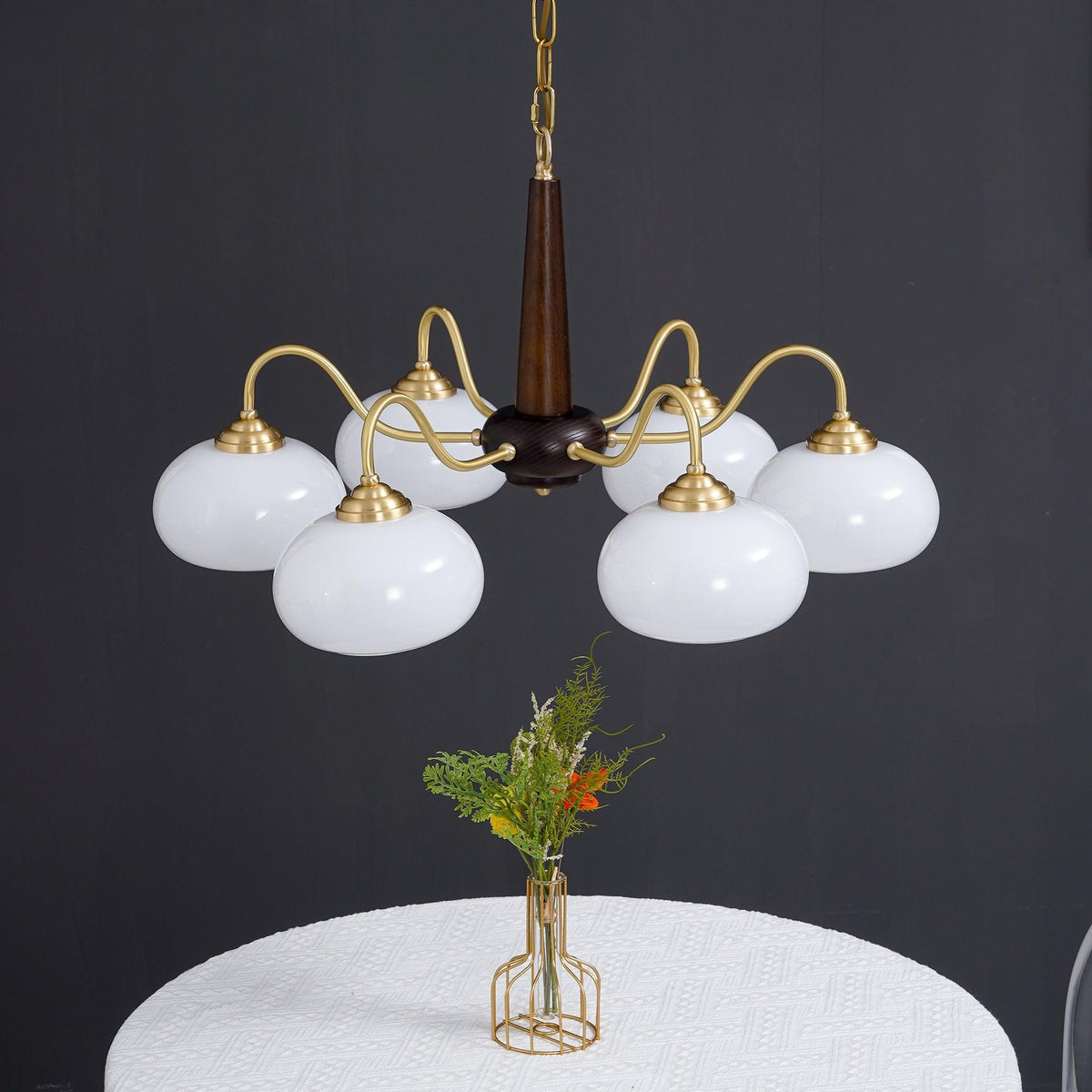 Against a charcoal backdrop, this Clérachic chandelier's white shades hang above a small posy of wildflowers.