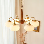 Dried pampas grass stands beneath this Clérachic chandelier, its brass arms catching light near a window.