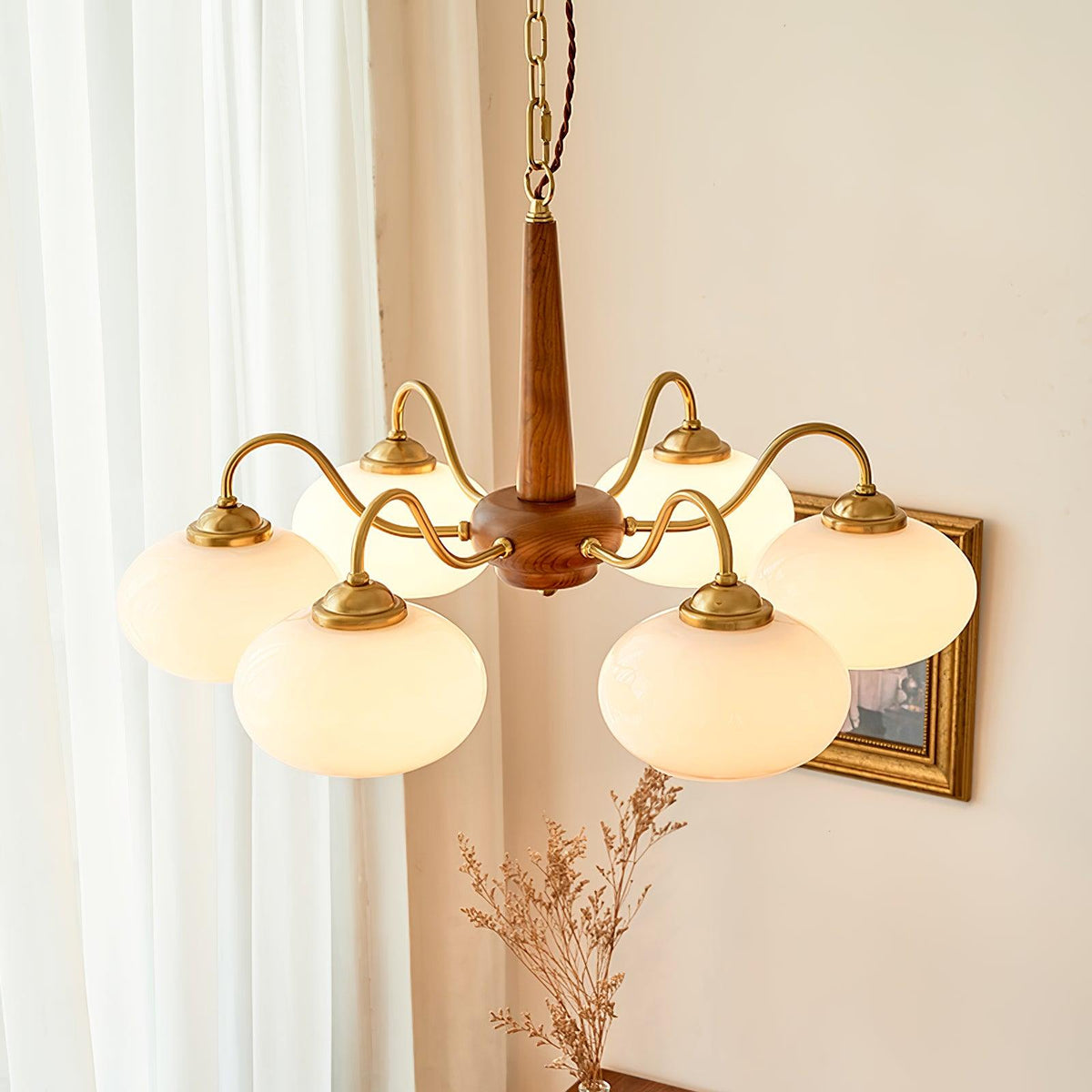Dried pampas grass stands beneath this Clérachic chandelier, its brass arms catching light near a window.