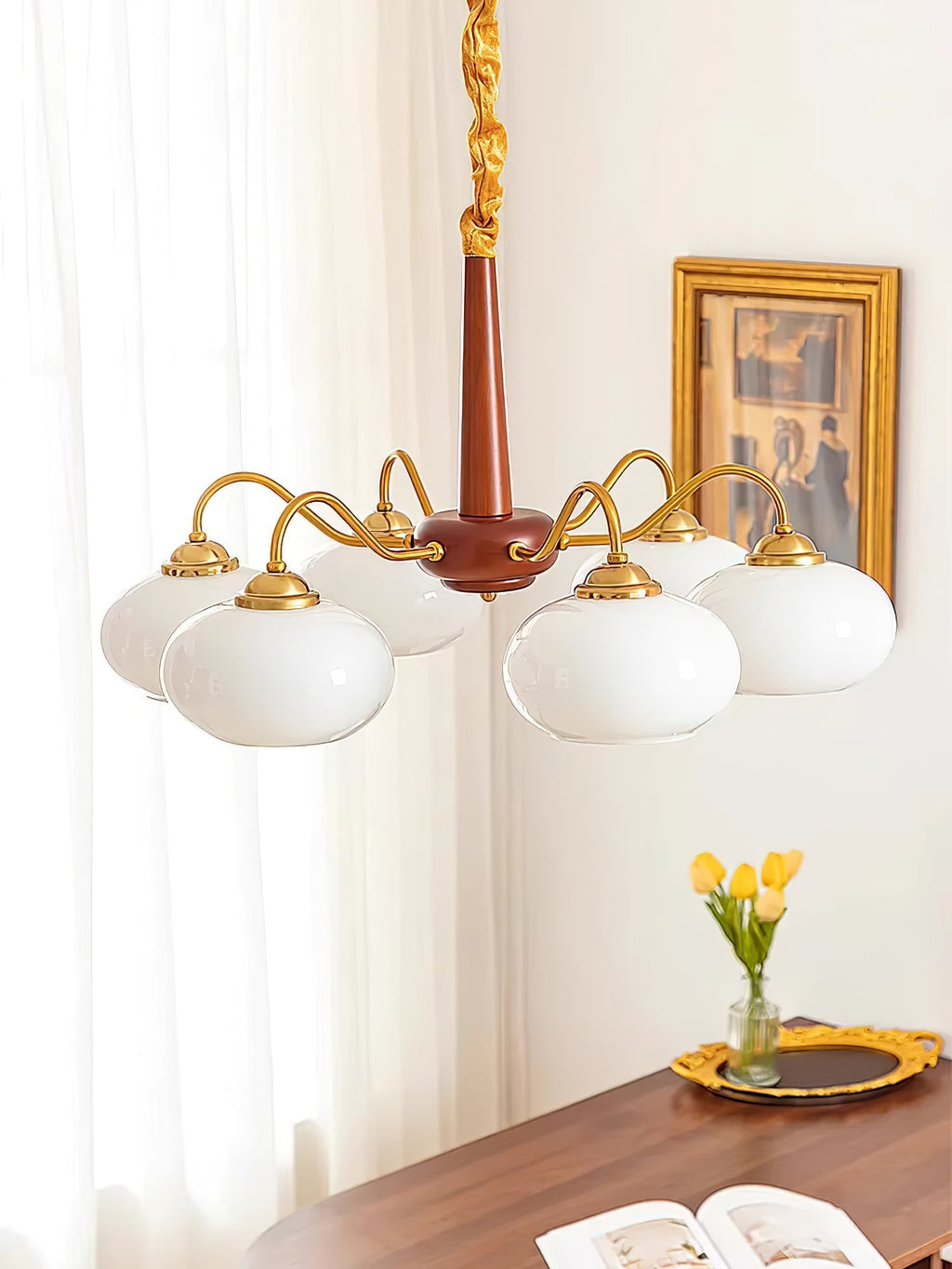 An open book rests on a table below this Clérachic chandelier's six white glass shades.