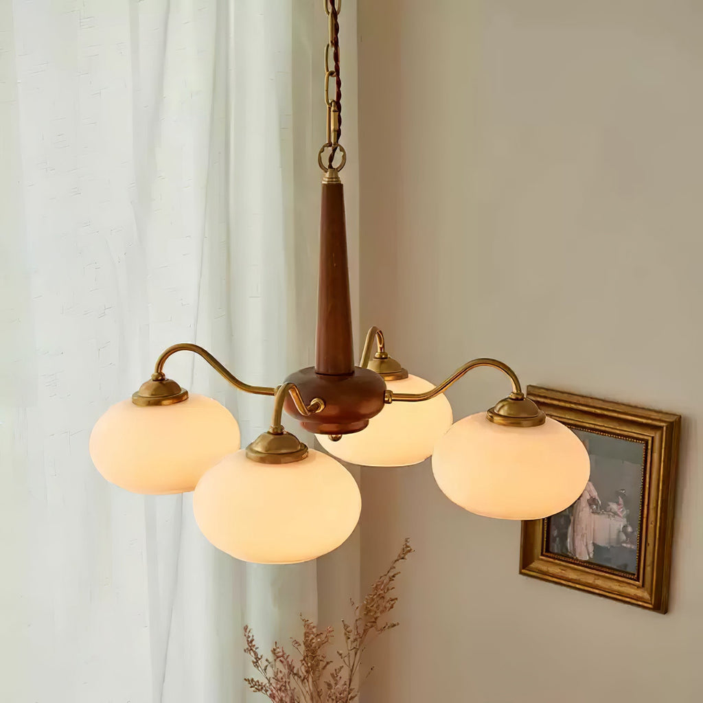 A gilt-framed countryside print hangs beside this Clérachic chandelier's four white glass shades.