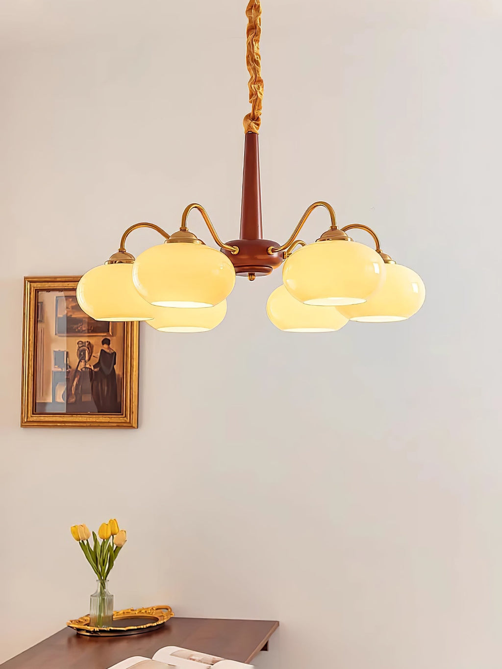 Yellow tulips on a woven tray sit below this Clérachic chandelier, beside a gilt-framed portrait.