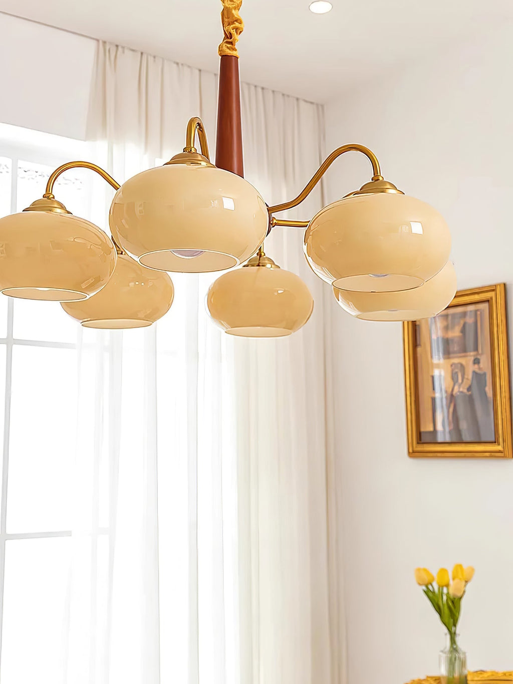 Seen from below, this Clérachic chandelier's cream shades hang near a sunlit curtain and a small framed print.
