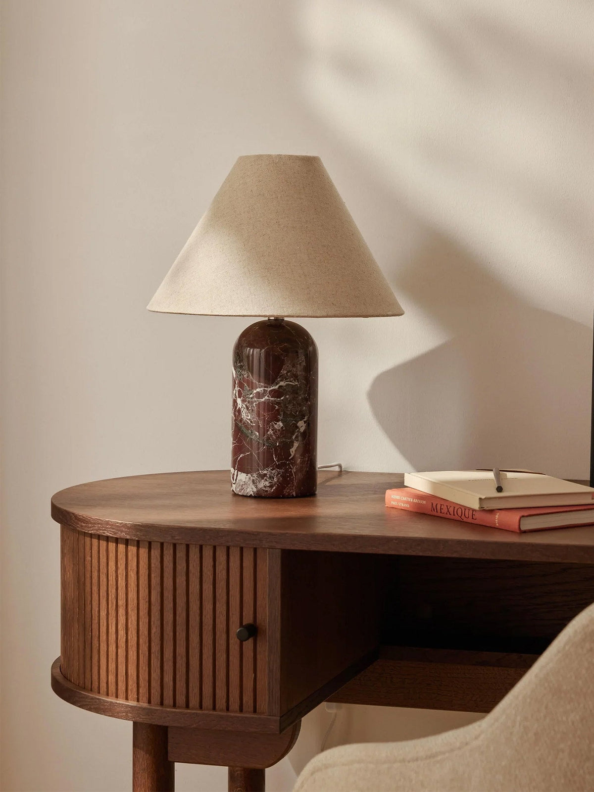 Clérachic lamp in a deep burgundy marble finish, lit on a rounded wooden nightstand beside a book.