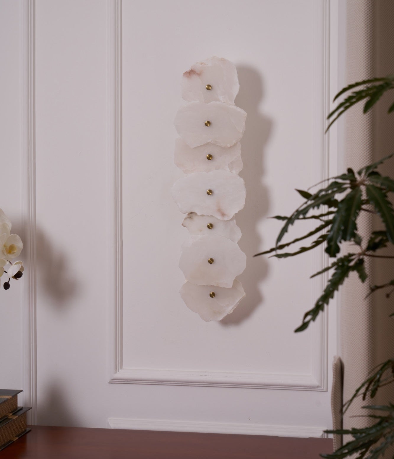 Unlit Alaeila alabaster wall light on a panelled wall, pale petal-shaped stones with brass studs.