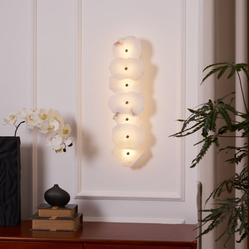 Seven-head alabaster wall lamp lit on a white panelled wall above a sideboard with an orchid.