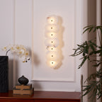 Seven-head alabaster wall lamp lit on a white panelled wall above a sideboard with an orchid.