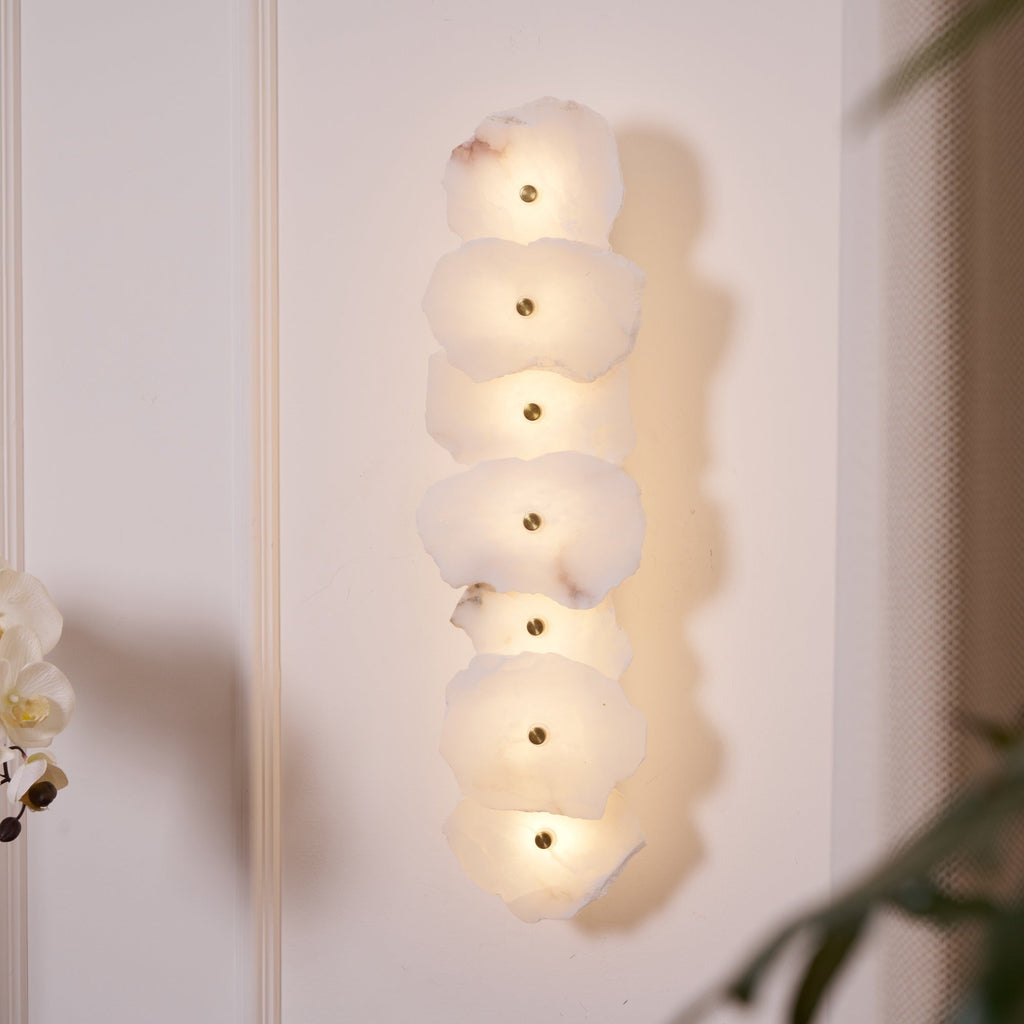 Close angled view of the lit alabaster wall lamp, each slab's chipped edge and brass stud in focus.