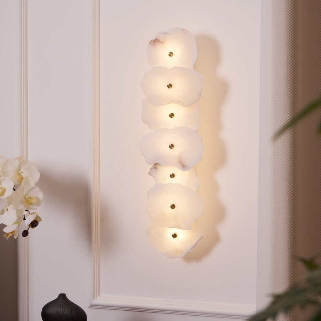 Seven stacked alabaster slabs lit warm, viewed from the side so the glow on the wall is visible.