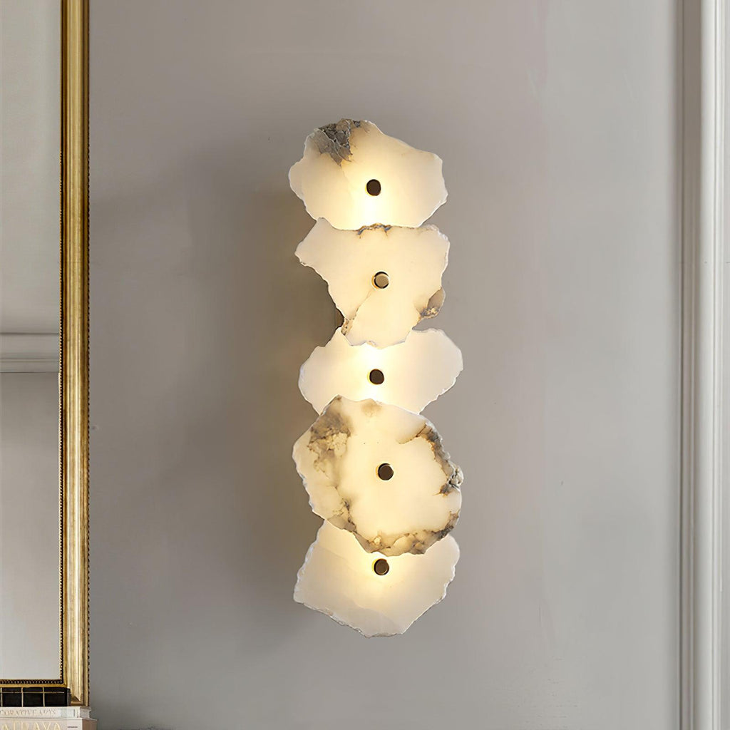 Five-head alabaster wall lamp lit beside a gilt-framed mirror on a soft grey wall, seen at an angle.