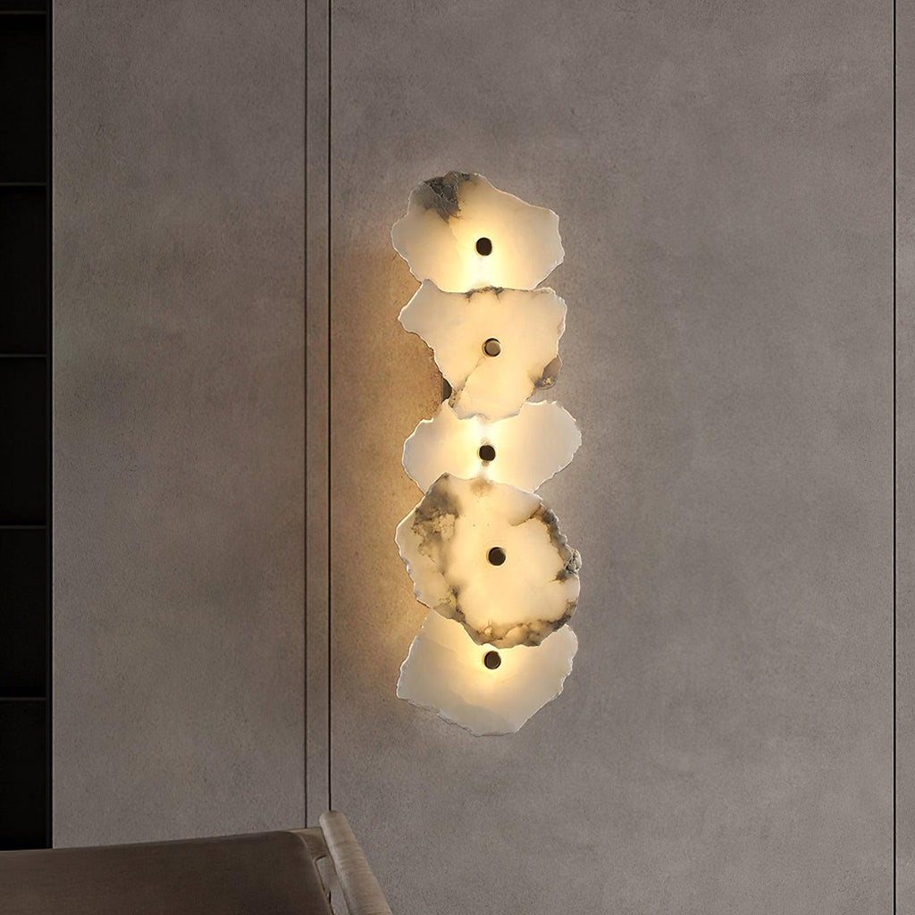 The alabaster wall lamp glowing against a dark plaster wall, its warm halo spilling onto the surface.