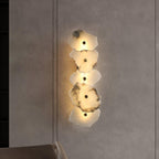 The alabaster wall lamp glowing against a dark plaster wall, its warm halo spilling onto the surface.