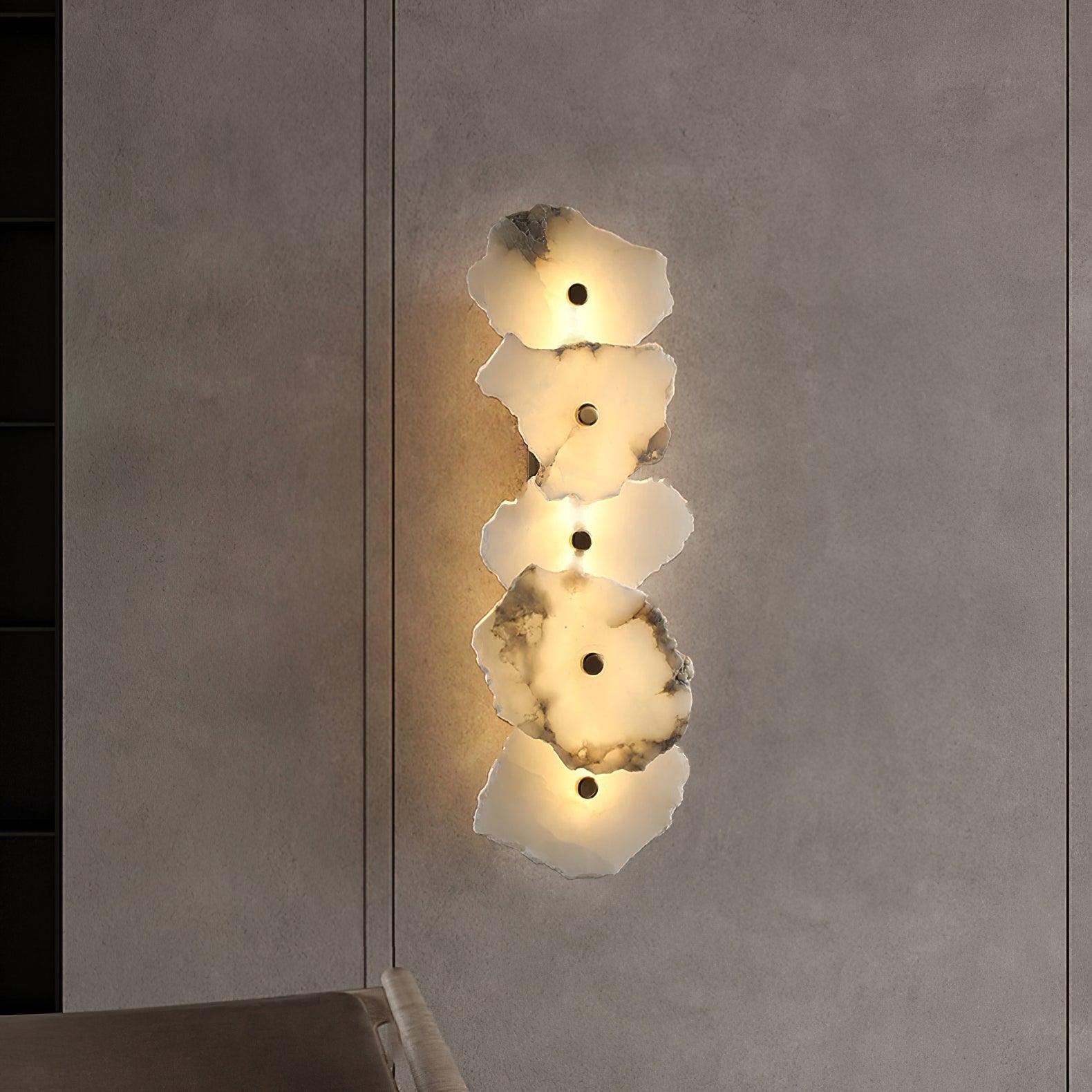 The alabaster wall lamp glowing against a dark plaster wall, its warm halo spilling onto the surface.