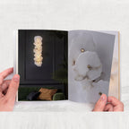 Hands holding an open lookbook: the lamp lit on a dark wall, and a close-up of the alabaster stone.