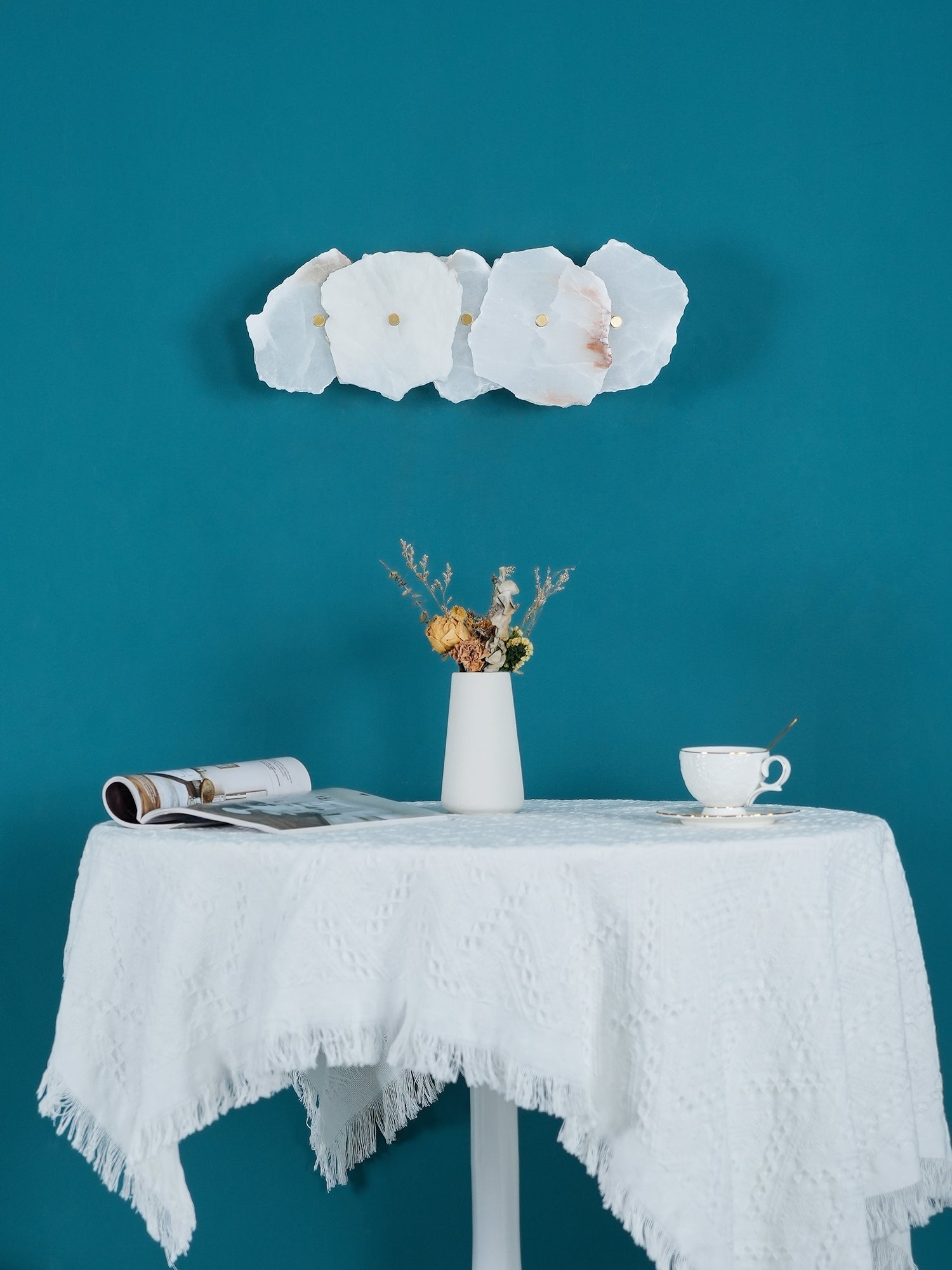 Alaeila alabaster wall light switched off in daylight, its pale stone petals against teal paint.