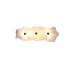 Three overlapping alabaster slabs lit warm, showing the lamp's compact horizontal three-head layout.