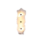 Three-head alabaster wall lamp stacked vertically, each stone slab lit warm and pinned by a brass stud.