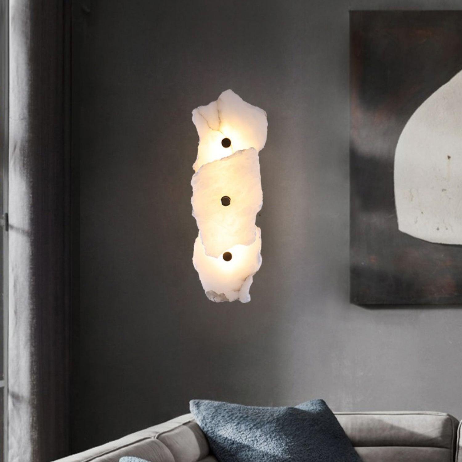 Three-head alabaster wall lamp lit on a charcoal wall above a sofa, beside a framed artwork.