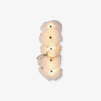 Vertical five-head alabaster wall lamp on a soft off-white background, warm light glowing between slabs.