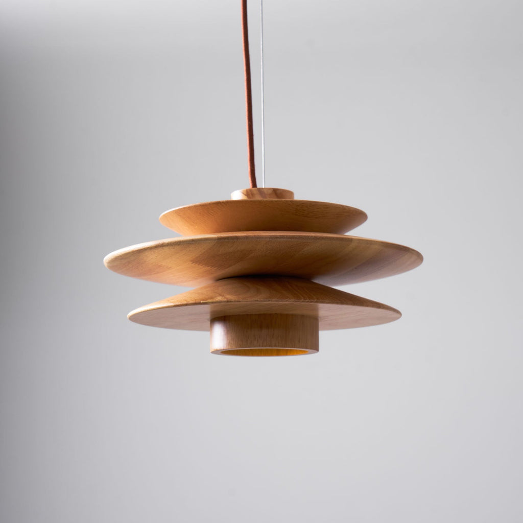 From the side, this Clérachic pendant in nature wood shows its interior diffuser glowing amber beneath the tiered discs.