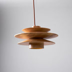 From the side, this Clérachic pendant in nature wood shows its interior diffuser glowing amber beneath the tiered discs.