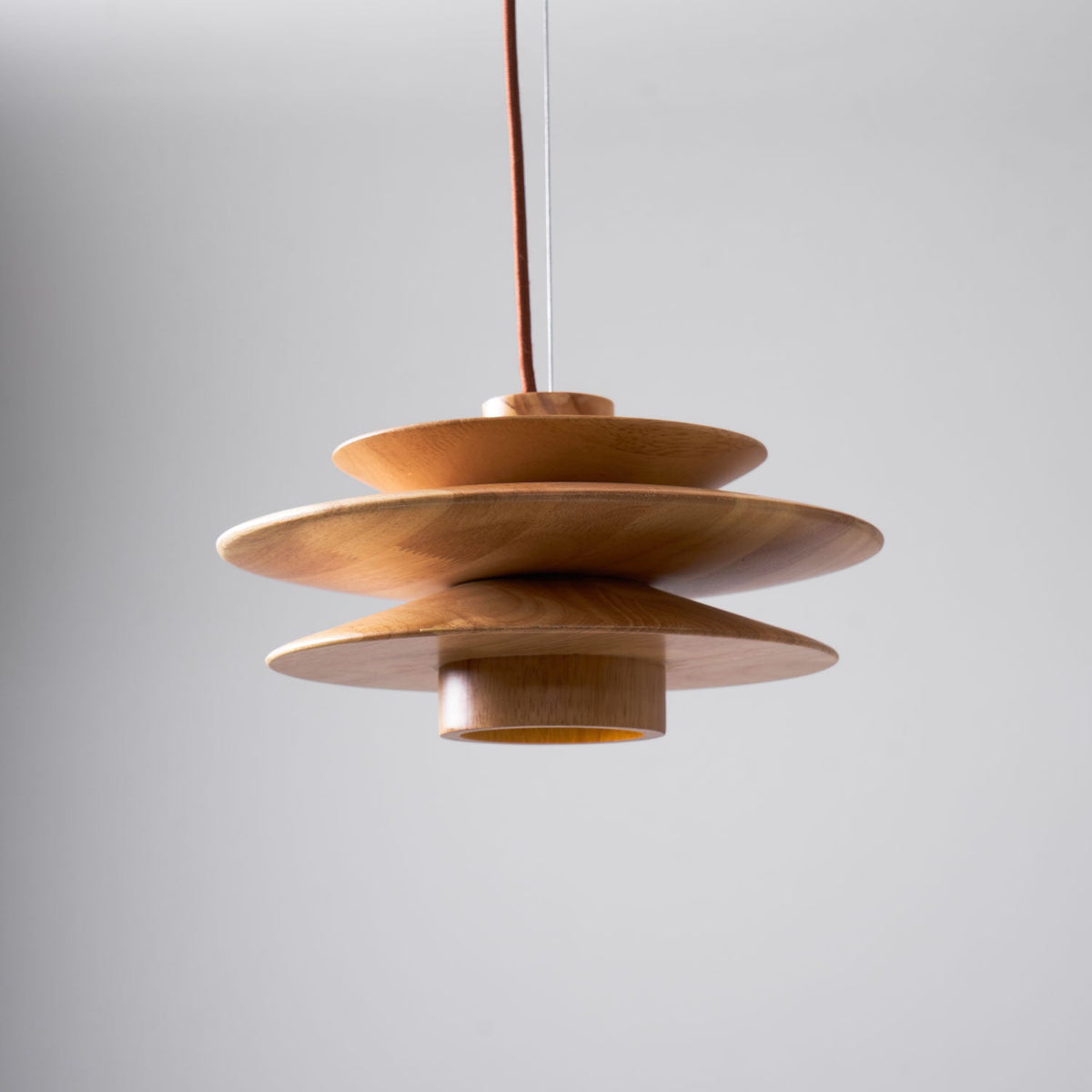 From the side, this Clérachic pendant in nature wood shows its interior diffuser glowing amber beneath the tiered discs.
