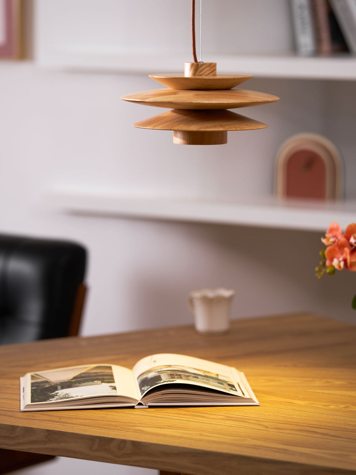 This Clérachic pendant in nature wood hangs above a wood desk with an open book and a black leather chair nearby.