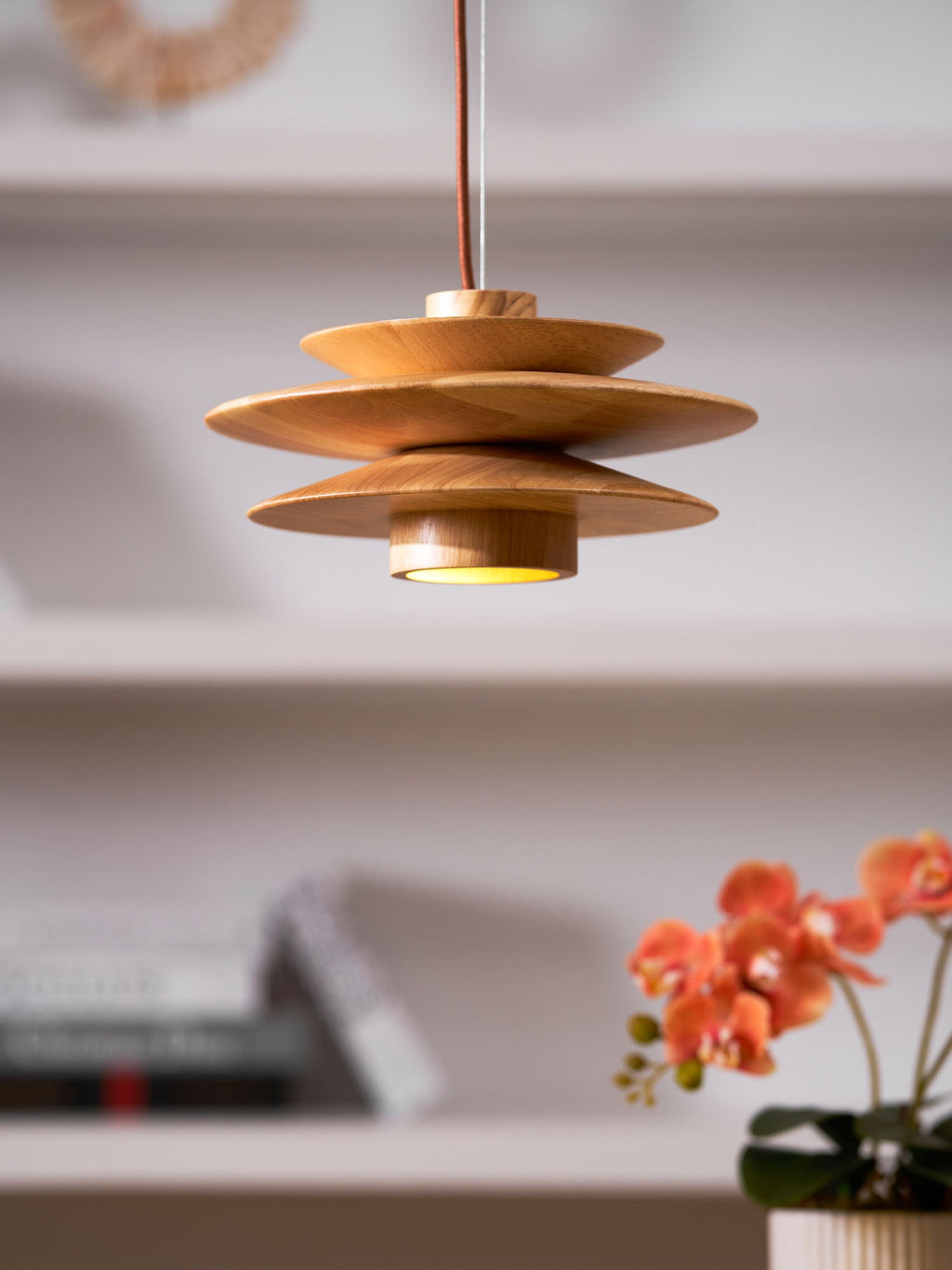 Glowing warmly above a desk, this Clérachic pendant in nature wood has an orchid and bookshelf softly blurred behind it.