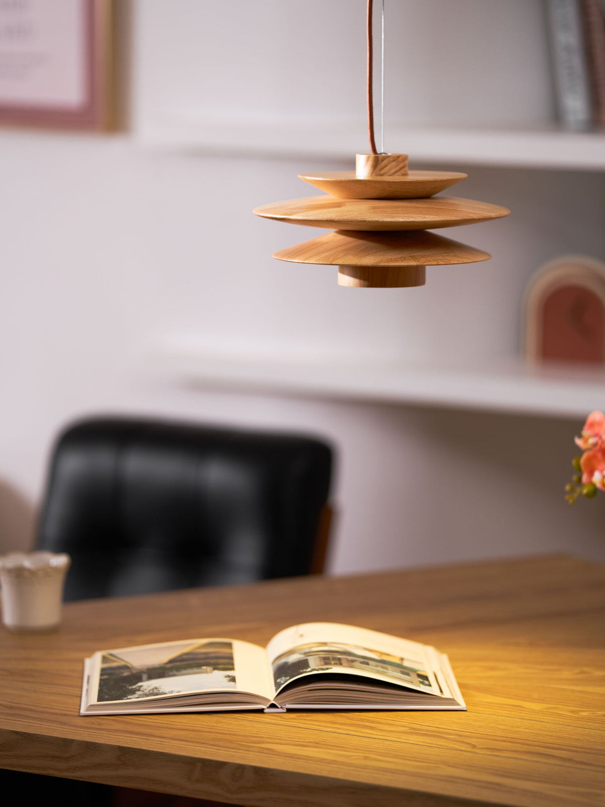 This Clérachic pendant lamp in nature wood is shown above an open book and a small orchid in a bright home office.