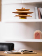 Above a desk with an open book, this Clérachic pendant in nature wood lights a softly lit study beside a black chair.