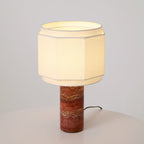 Set against a bare backdrop, this Clérachic table lamp's red travertine column rises from a plain white surface.