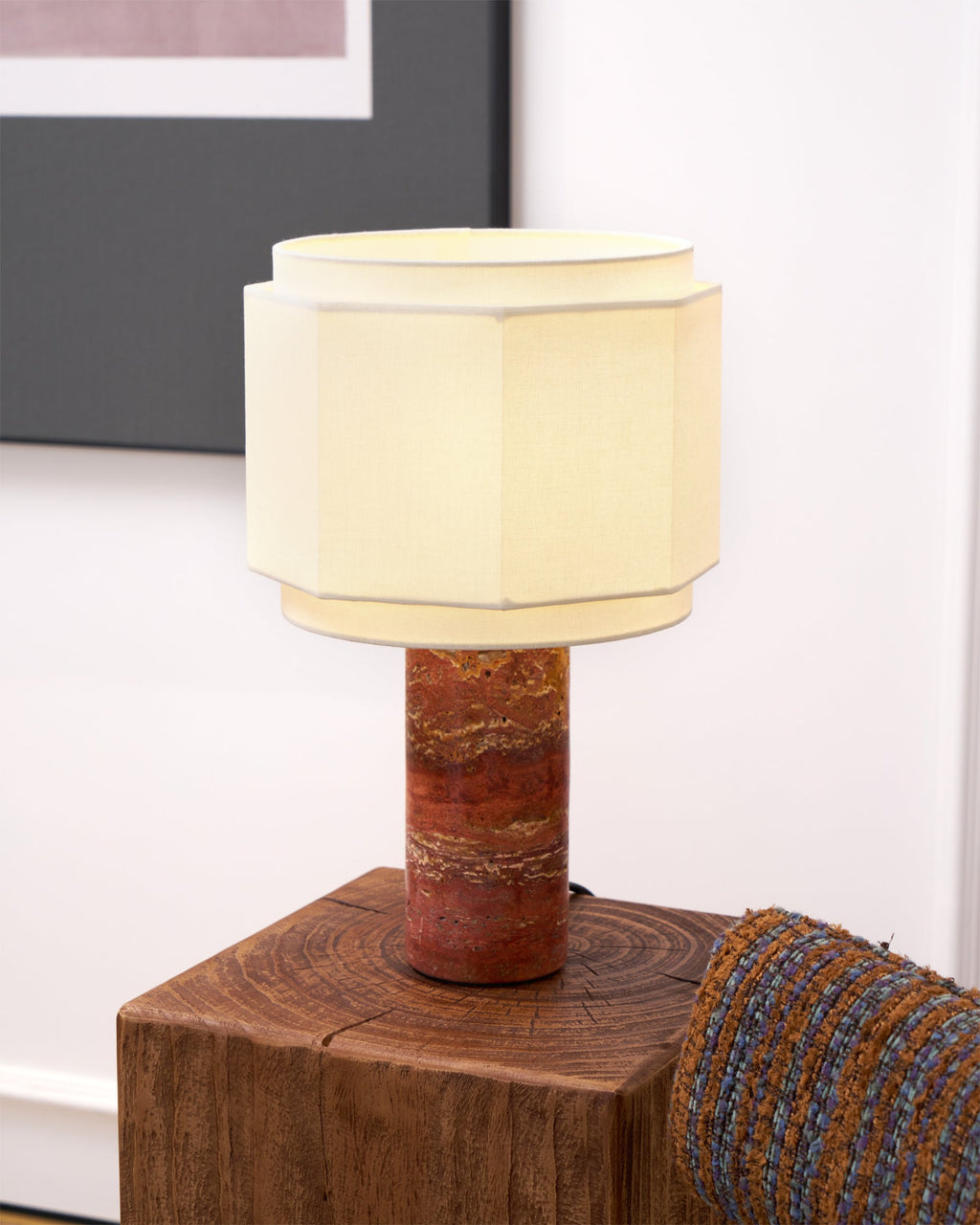 This Clérachic table lamp glows on a wood block, framed art and a woven chair arm blurred in the background.